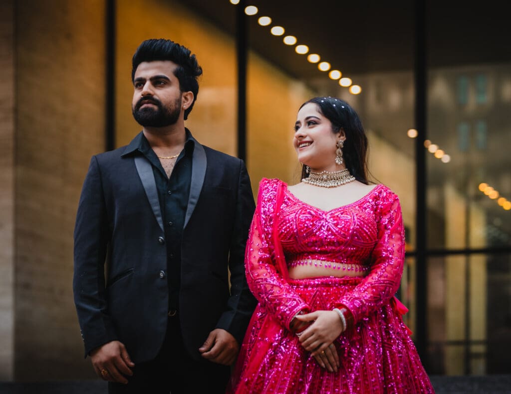 Candid downtown Toronto wedding portrait of an Indian couple, groom in black suit and bride in a bright pink lehenga, captured in a modern city setting.