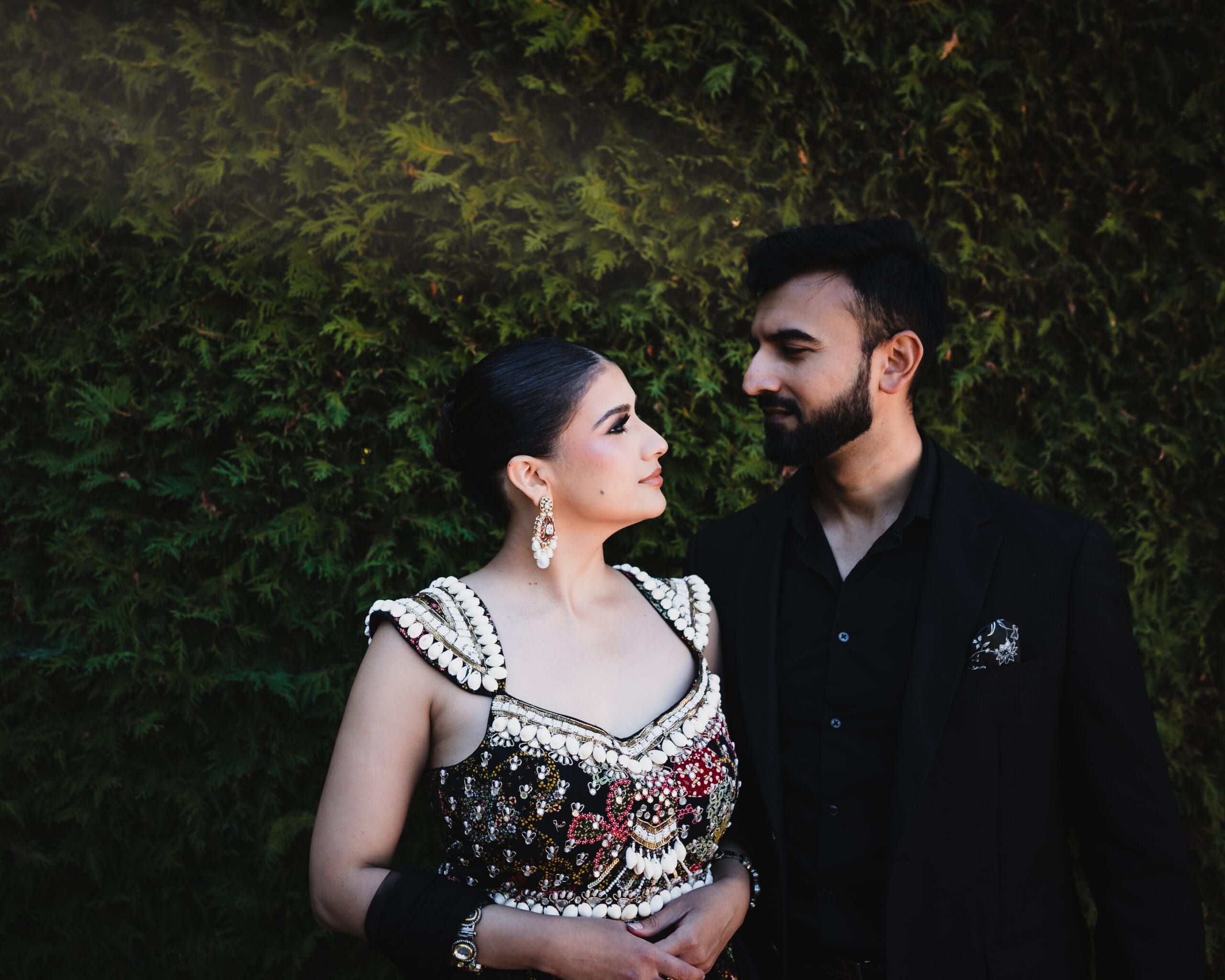 Elegant South Asian wedding couple portrait at Parkwood Estate, Oshawa — bride in embellished lehenga looking at groom by evergreen hedge