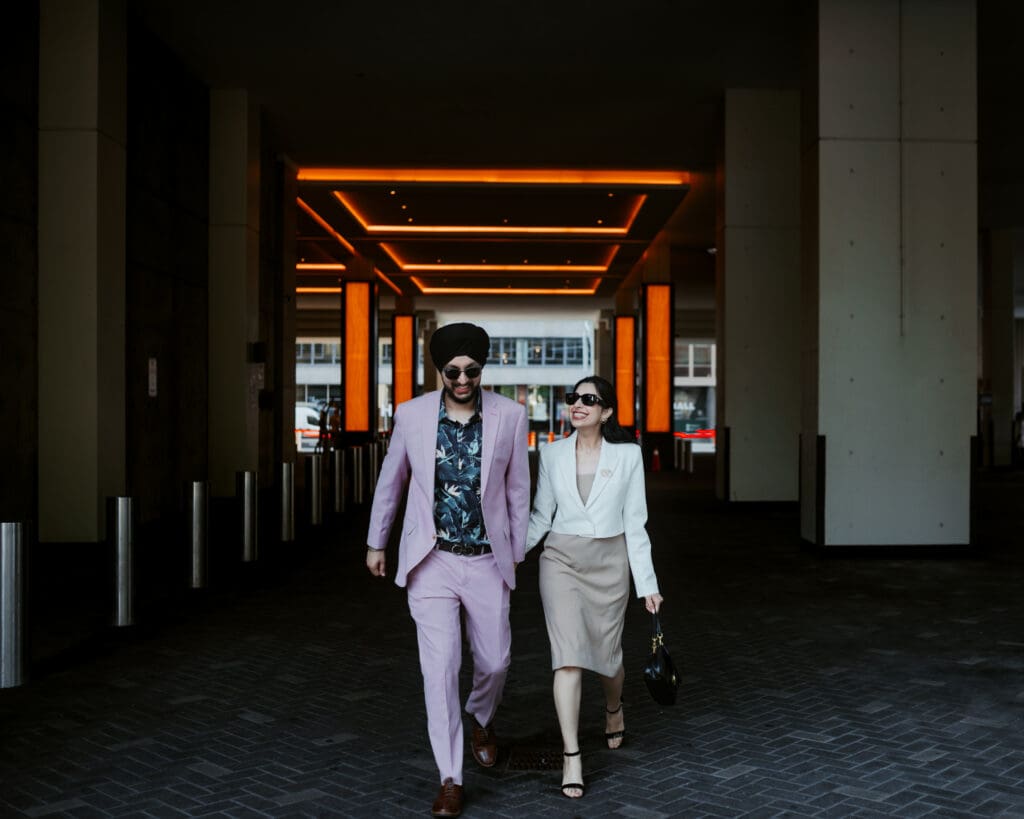 Punjabi couple walking hand in hand in downtown Toronto, stylish pre-wedding photoshoot under modern lobby lights.