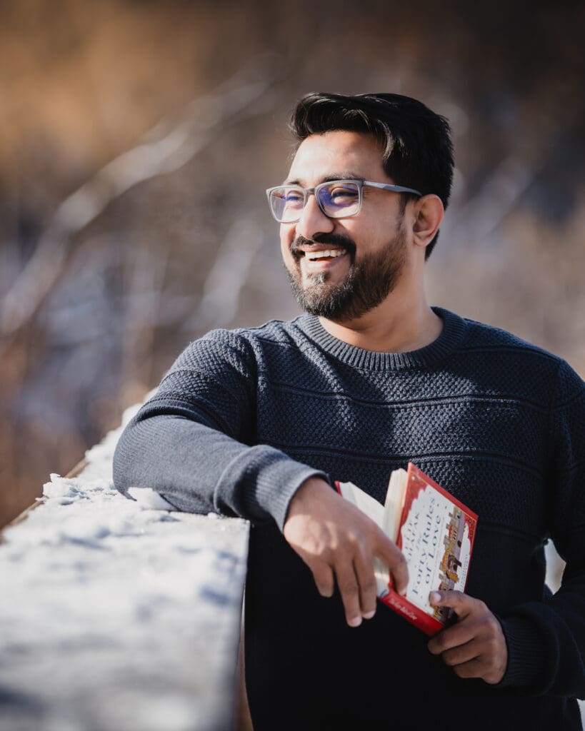 Portrait of a Toronto wedding photographer smiling outdoors in winter light, wearing glasses and holding a book, with soft blurred background.