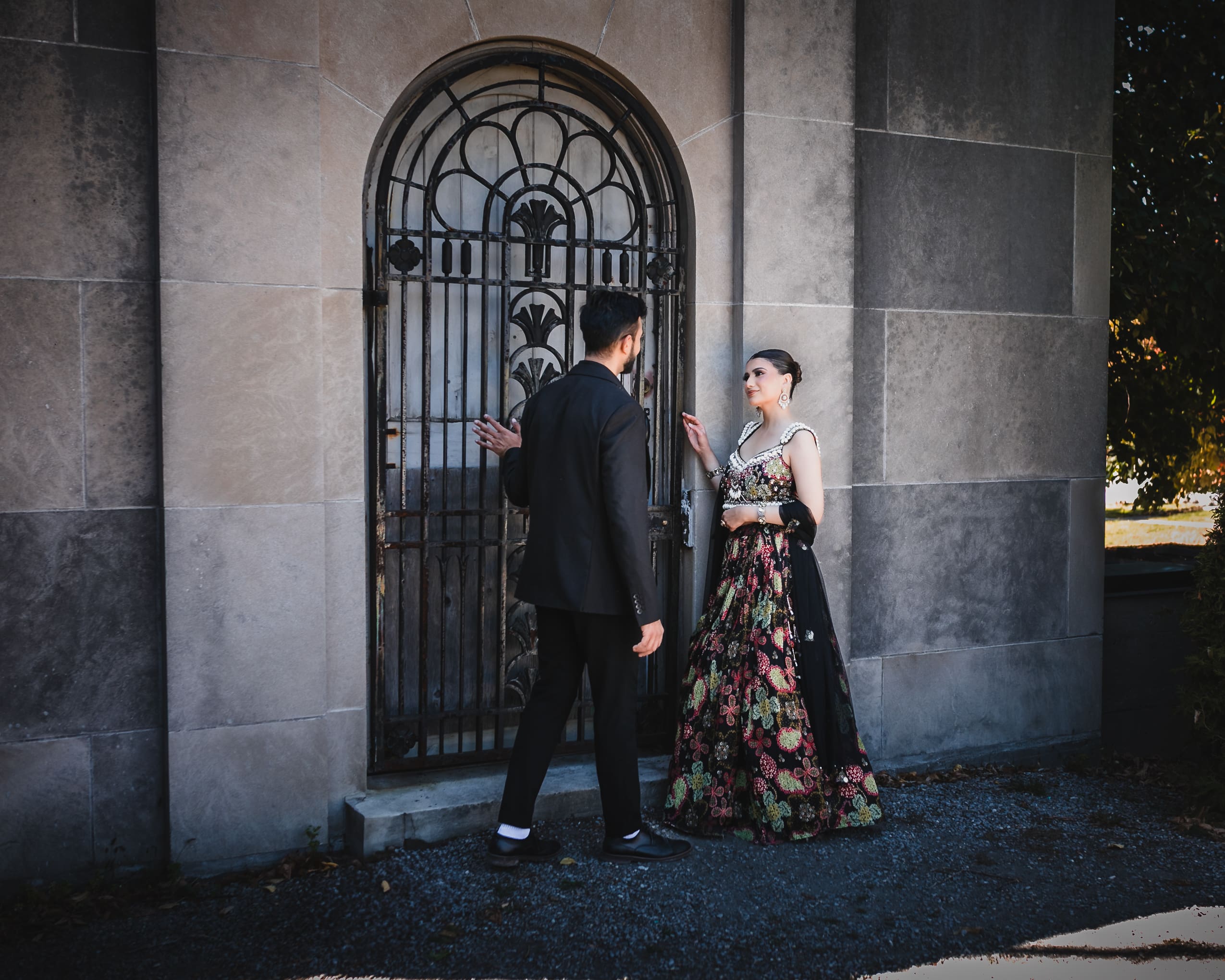 Wedding couple portrait by an ornate iron gate at Parkwood Estate in Oshawa, Ontario, bride in embroidered lehenga and groom in black suit sharing a quiet moment, cinematic estate wedding photography near Toronto and GTA.