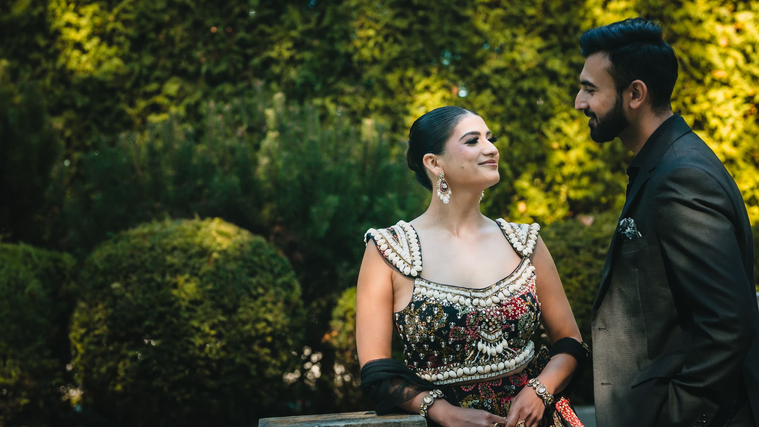 Wedding couple portrait in the gardens at Parkwood Estate in Oshawa, Ontario, bride in embellished lehenga smiling at groom in dark suit, cinematic outdoor wedding photography near Toronto and GTA.