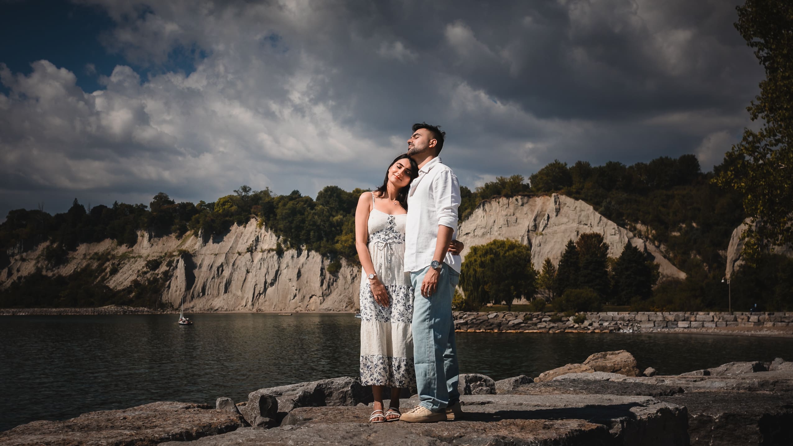 Engagement couple portrait at Scarborough Bluffs in Toronto, standing on rocky shoreline with dramatic cliffs and Lake Ontario behind them.