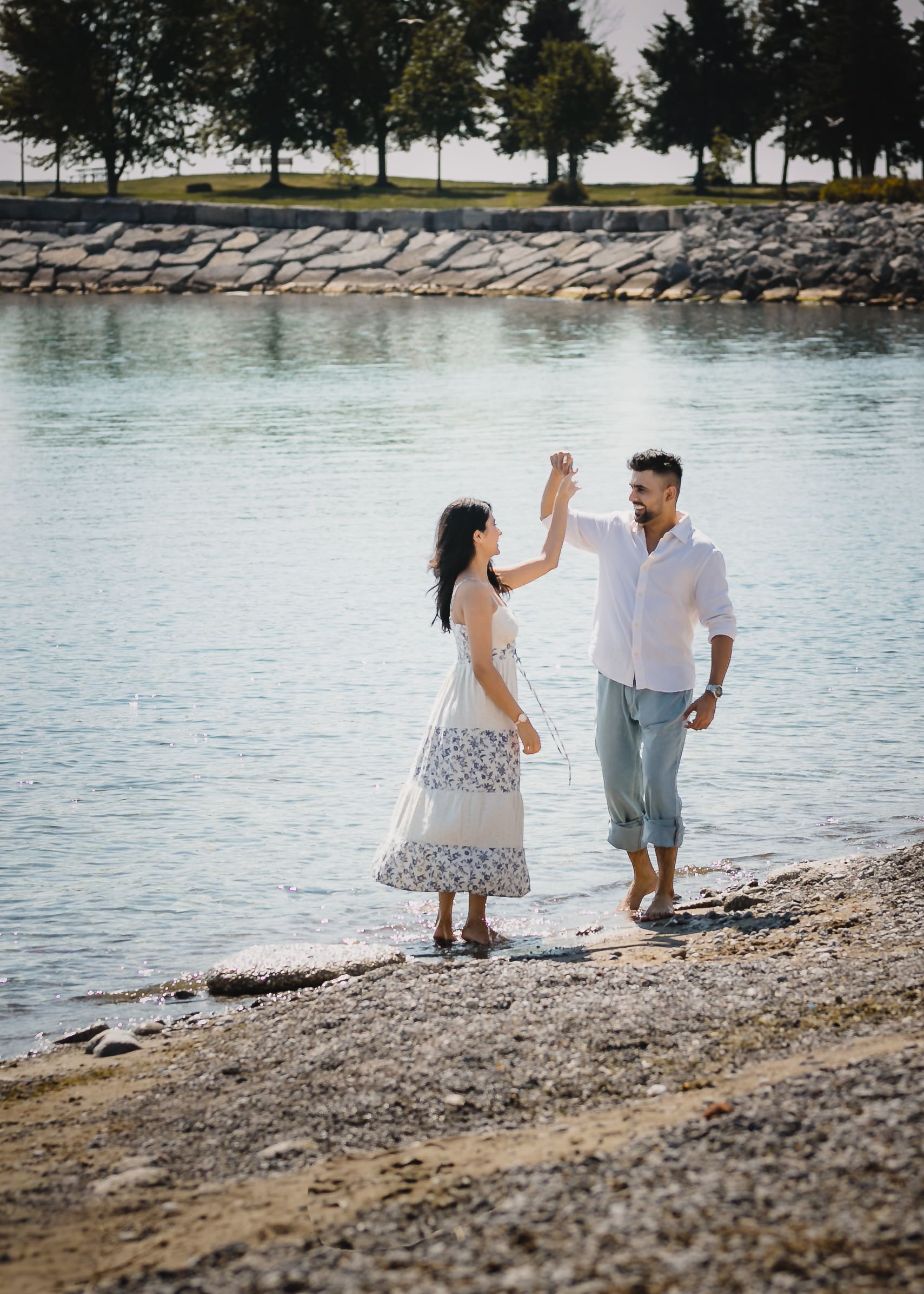 Pre-wedding couple twirling barefoot at the Scarborough Bluffs shoreline in Toronto, Ontario, candid romantic moment by the water.