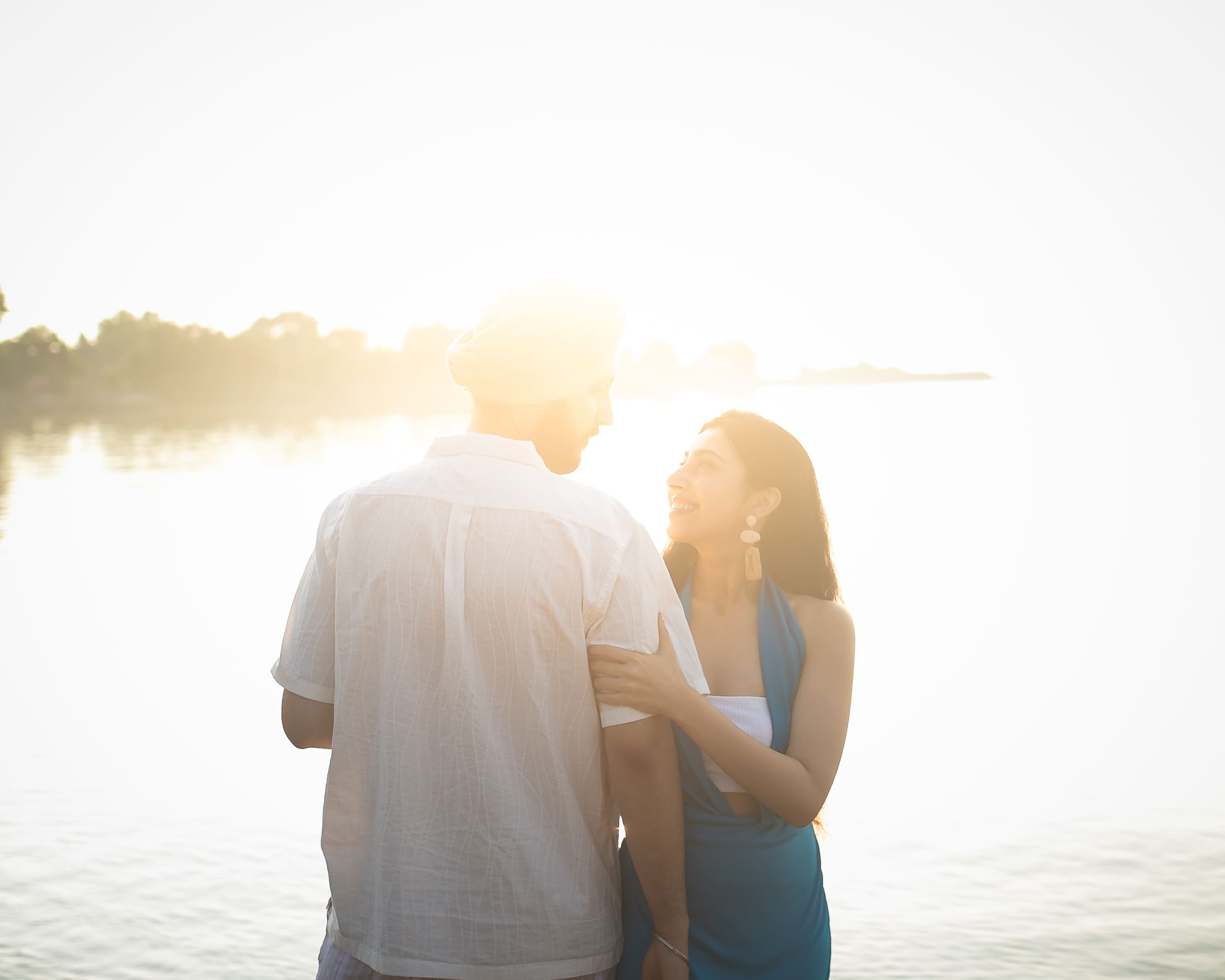 Backlit pre-wedding couple portrait at Scarborough Bluffs in Toronto, sun flare over Lake Ontario as they hold each other by the water.