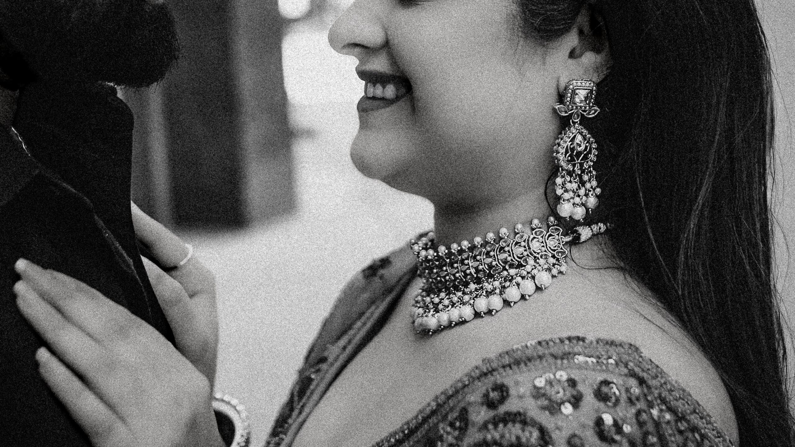 Black and white close-up of a South Asian bride smiling with detailed bridal jewelry including chandelier earrings and a statement choker necklace, captured in a cinematic Toronto wedding photography style.